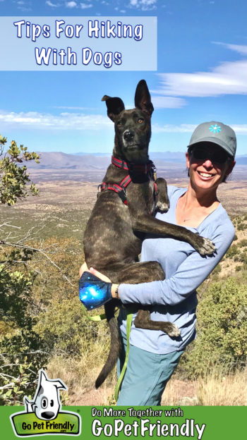 Woman holding dog on a pet friendly hiking trail with mountains in the background