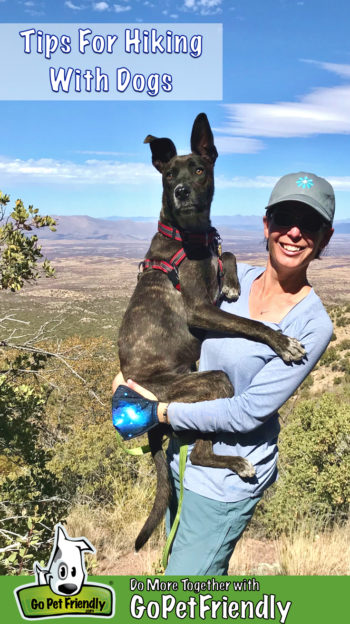 Woman holding a dog on a pet friendly hiking trail with mountains in the background