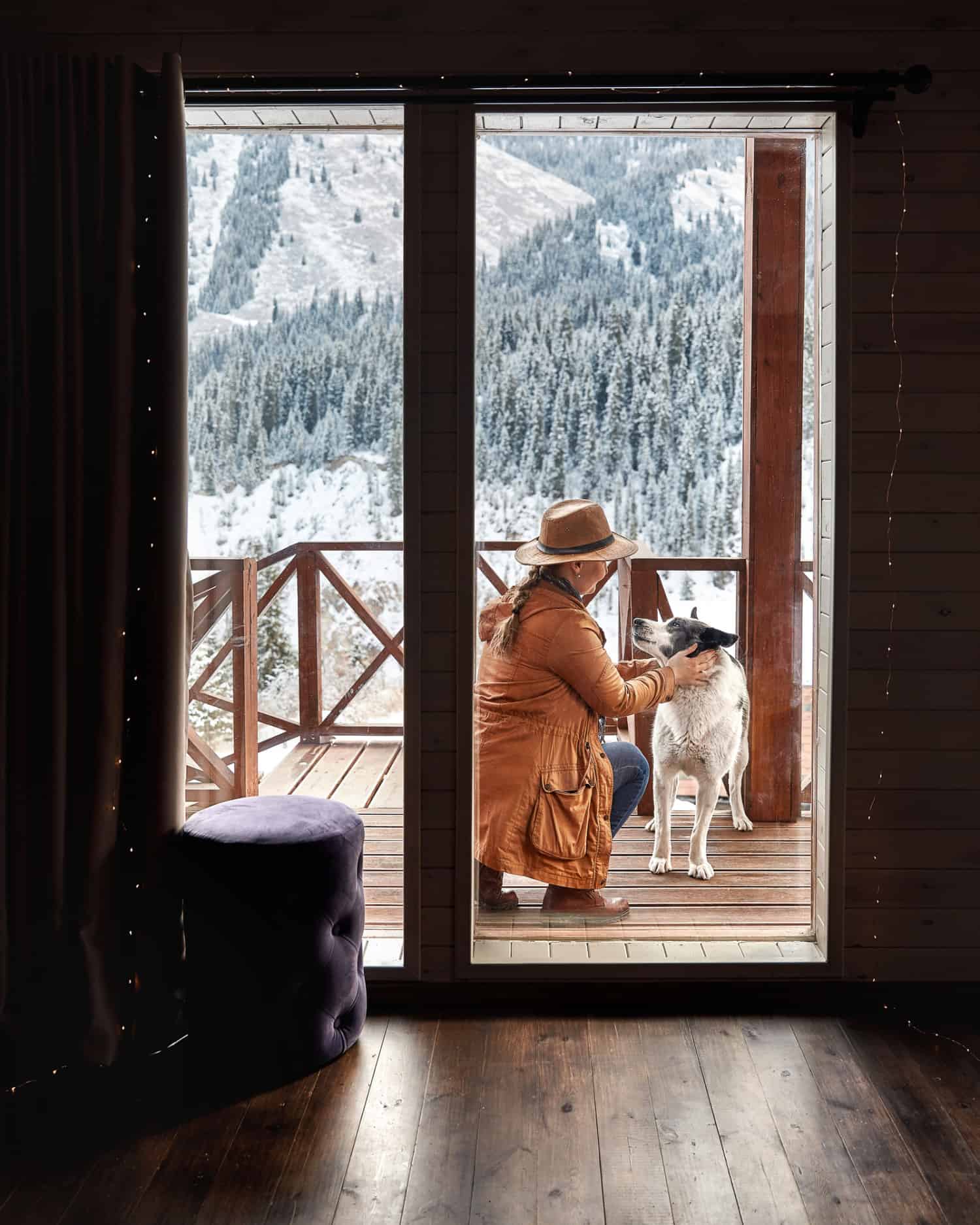 A woman in a hat plays with her dog on the deck of a pet-friendly vacation property in winter