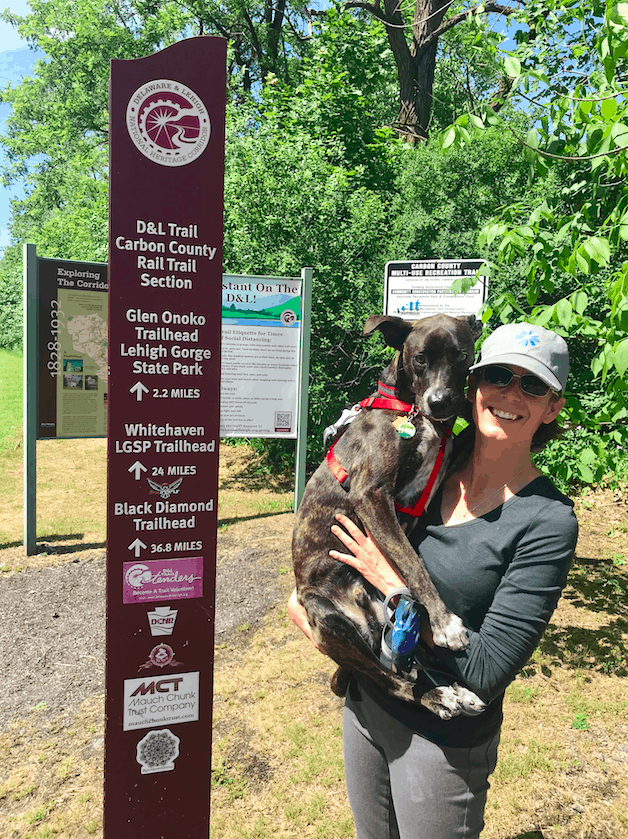 Woman holding brindle dog beside a trail sign in Jim Thorpe, PA