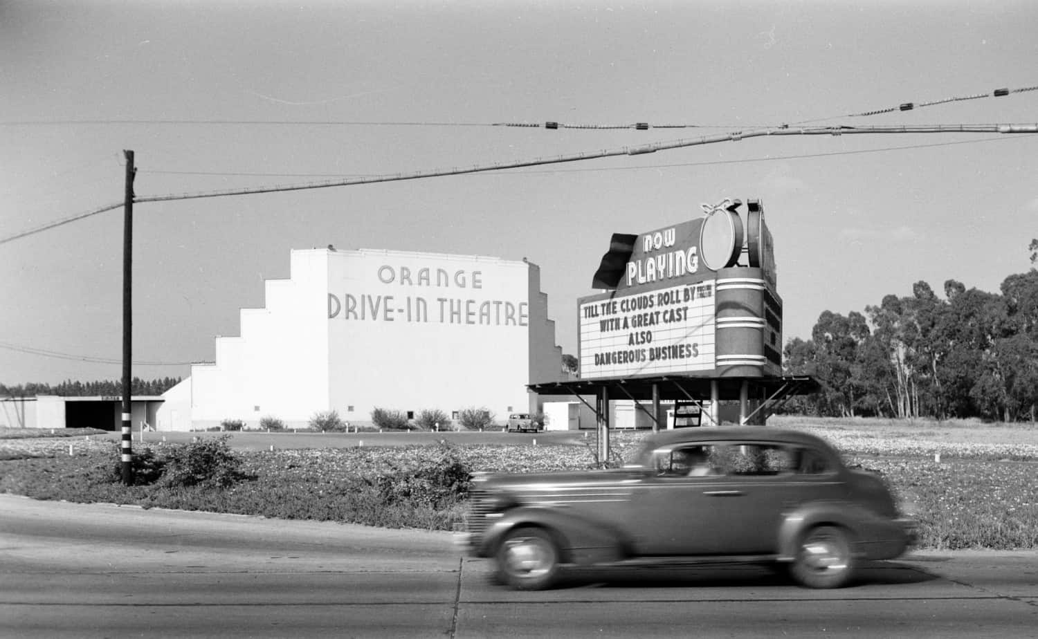 Old car driving by Orange Drive-In movie .