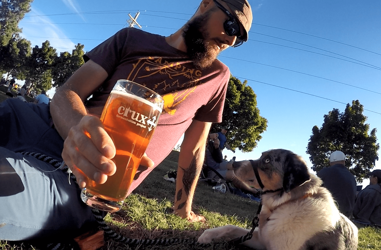 Man and dog sitting on the grass with a glass of kombucha at pet-friendly restaurant, Kebaba, in Bend, Oregon