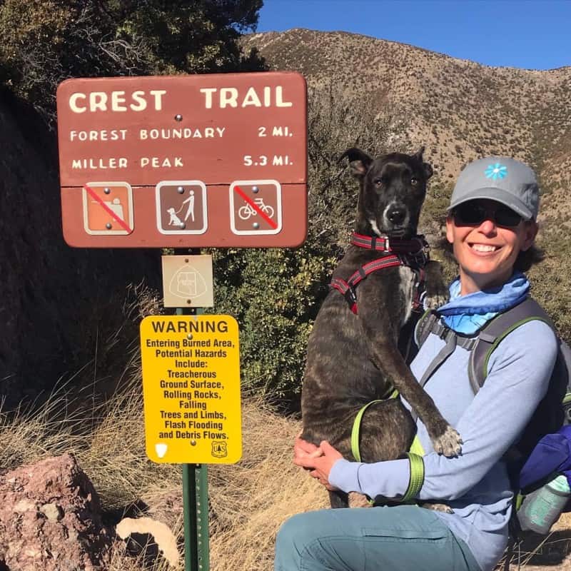 Woman holding dog beside sign for dog friendly Crest Trail at Coronado National Monument near Tucson, AZ 