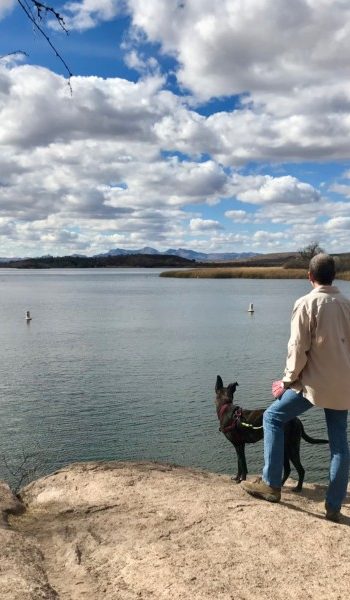 Man and dog overlooking a lake near Tucson, AZ with mountains in the distance
