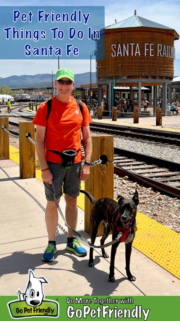 Happy man and smiling brindle dog in pet friendly Santa Fe, NM with a sign for the Santa Fe Railway in the background