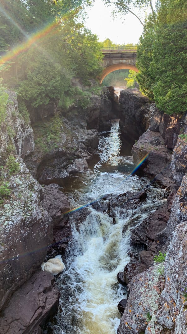 A river rushes through a gorge with bridge and trees in the background at Temperance River State Park on the North Shore in Minnesota