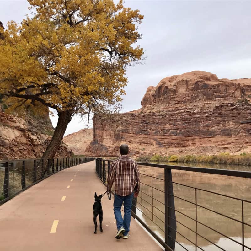 Man and dog walking along the Colorado River on the Moab Canyon Pathway near Moab, UT