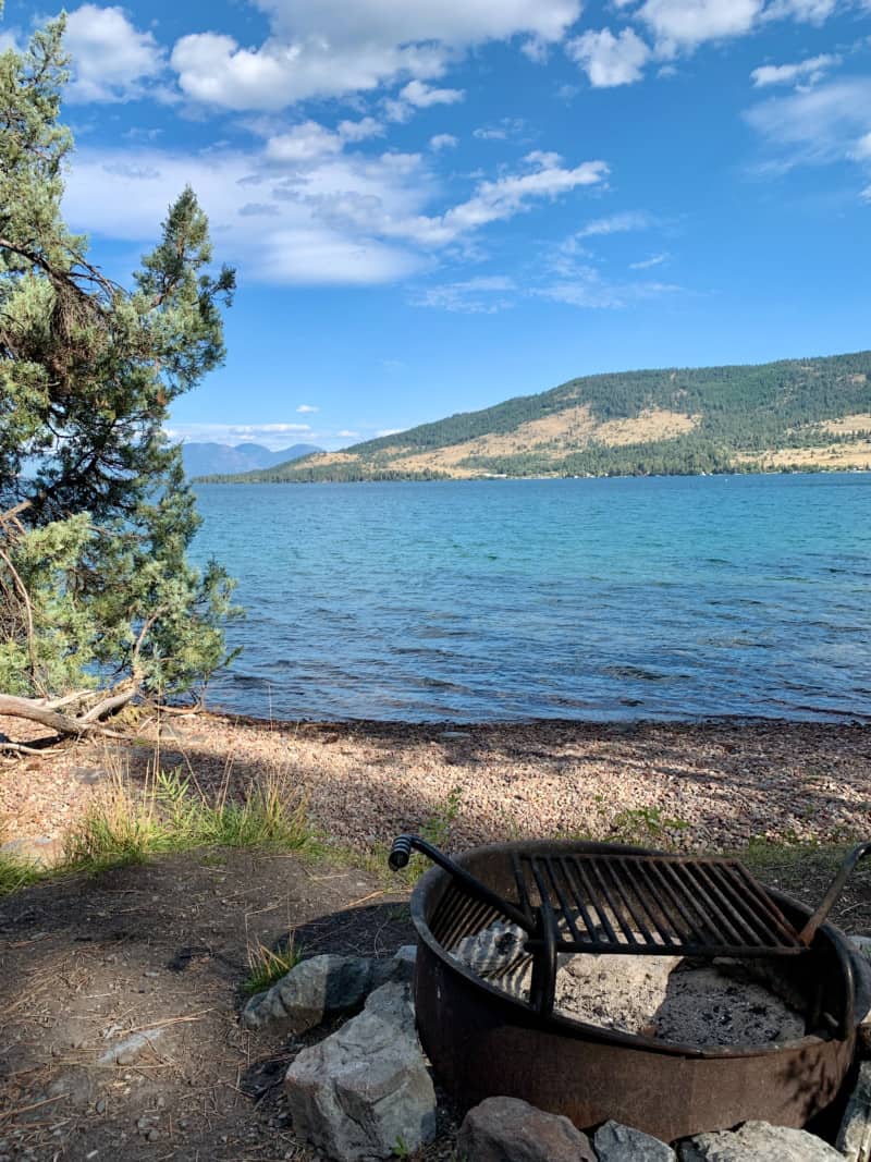 A fire pit on the shoreline of a lake with a forested hill in the background