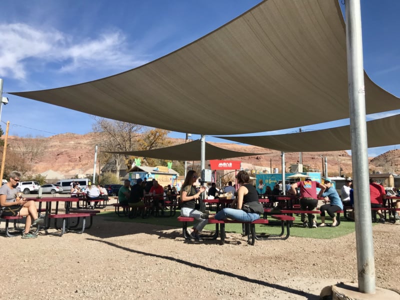 People sitting on shaded picnic tables at Moab Food Truck Park in Moab, UT