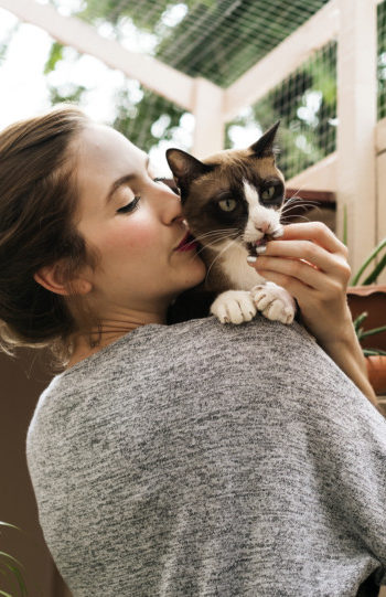 Woman snuggling calico cat in a sunroom