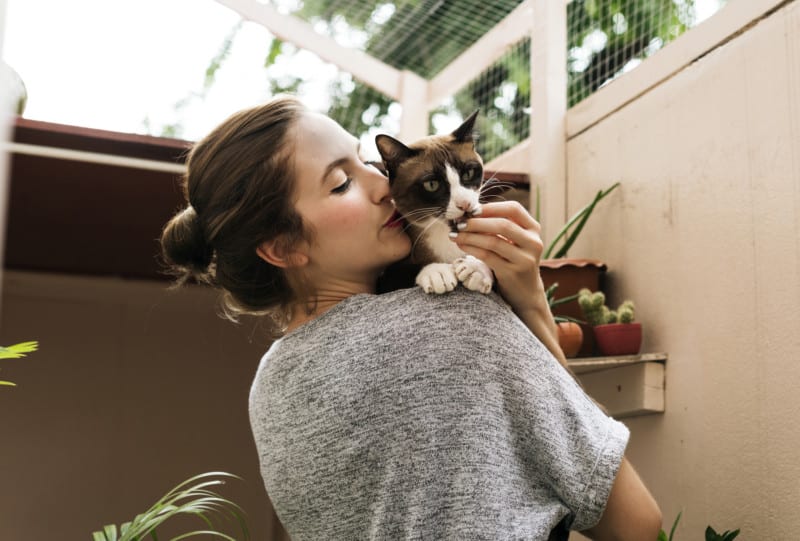 Woman snuggling calico cat in a sunroom