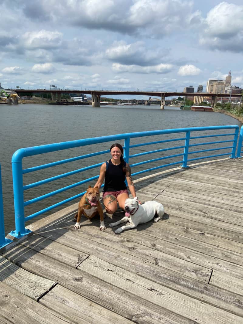 Two dogs and their owner walking down the paved walking path along the Mississippi River in Saint Paul, Minnesota