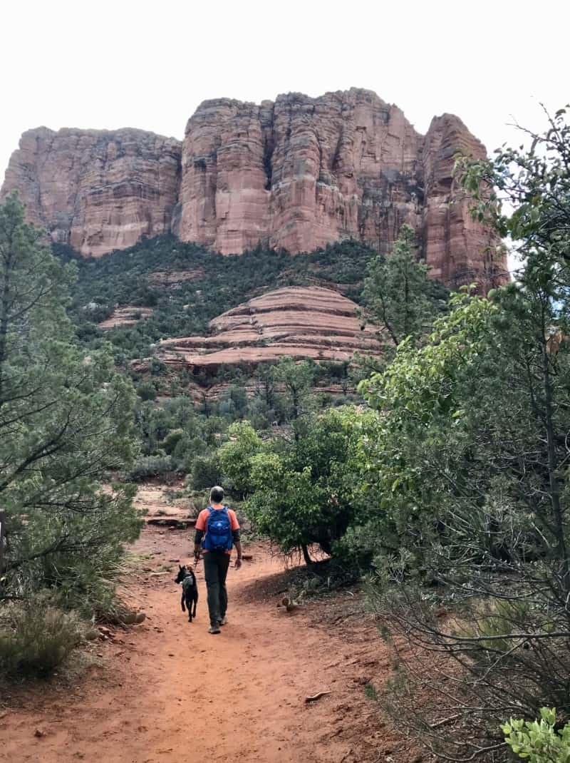 Man and dog walking a pet friendly trail in Sedona, AZ with Courthouse Butte in the background