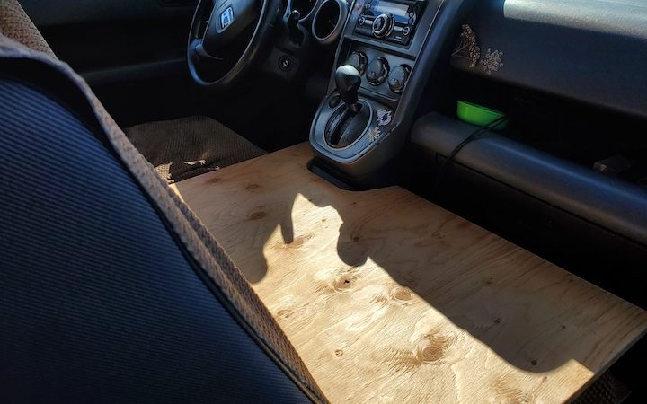 Showing a plywood cutout to go over front seats of vehicle to make a bed for a pet.