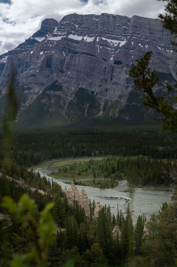 Landscape image of Banff. Hoodoos, forest, glacial river and enormous mountain are seen.