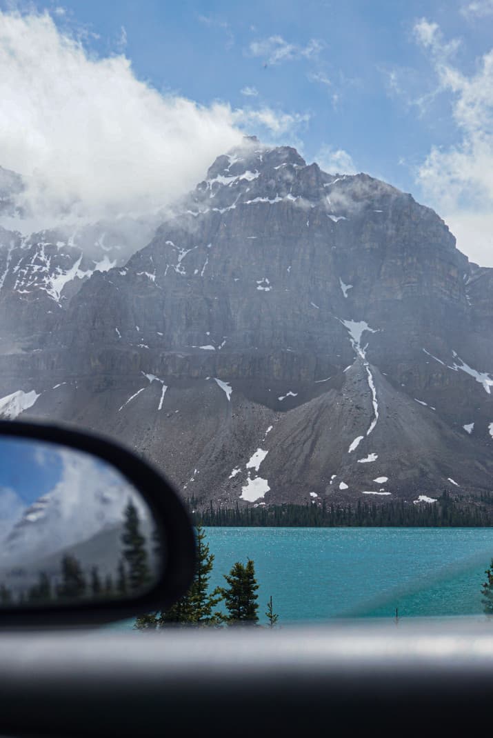 View of snowy mountains and bright blue lake framed by a car window in Banff.