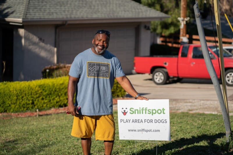African American man standing in front of house with a sign marking a  Sniffspot private off-leash dog park