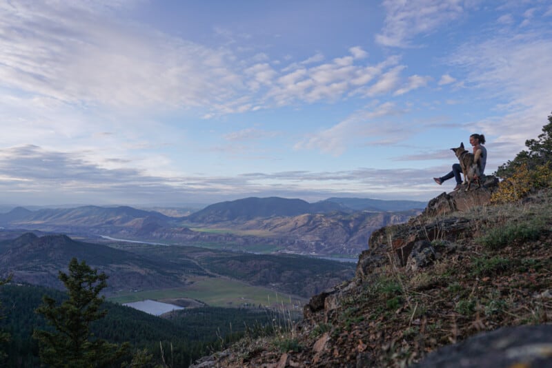 Hiking in Kamloops, BC. Woman and her dog sitting together on a rocky mountain overlooking the desert hills below.