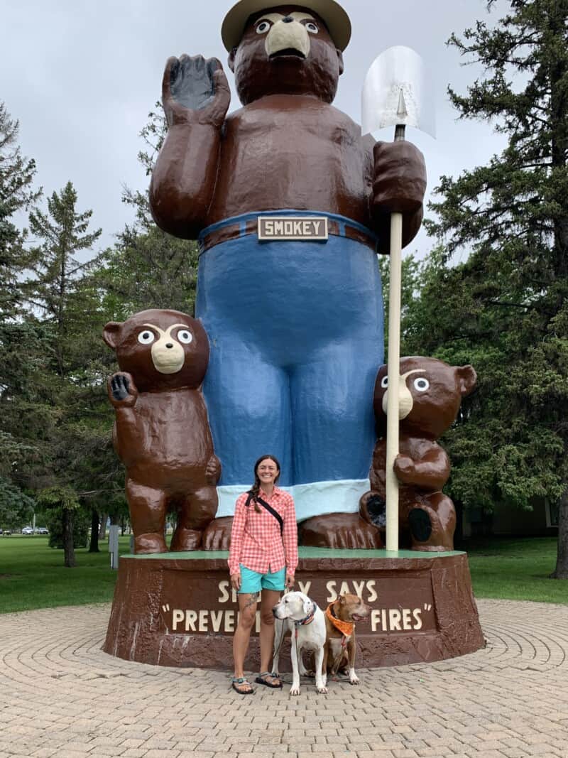 A woman and two dogs posing in front of a 26-foot tall Smokey the Bear Statue in park in International Falls
