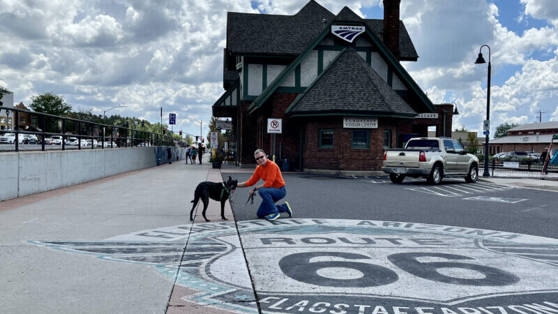 Man and a dog on the Route 66 sign painted on the parking lot at the Visitor Center in Flagstaff, AZ