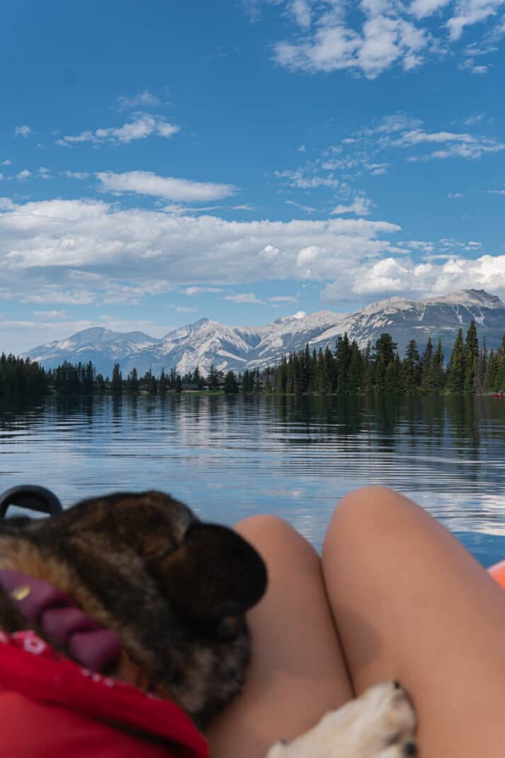 Girl and her dog floating on a raft in Lac Beauvert in Jasper. They are looking out towards the lake and snowy peaks.