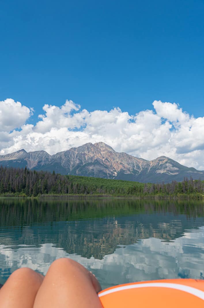 View of Pyramid Mountain reflecting into Patricia Lake in Jasper. A woman's legs floating on a raft are in the foreground.