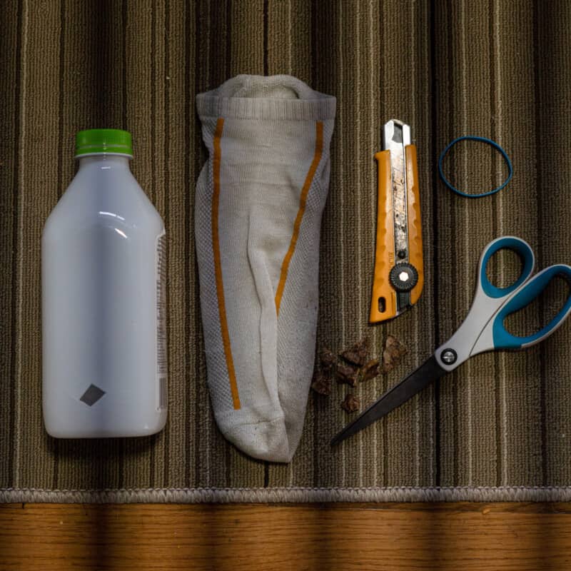 A flat lay of supplies to make an enrichment game for dogs. Plastic bottle, sock, scissors, rubber band and treats.