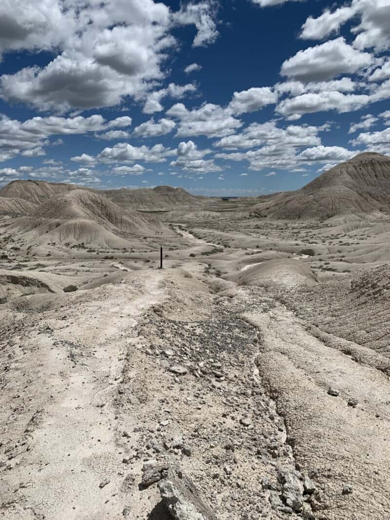 A trail marker can be seen ahead in the badlands.