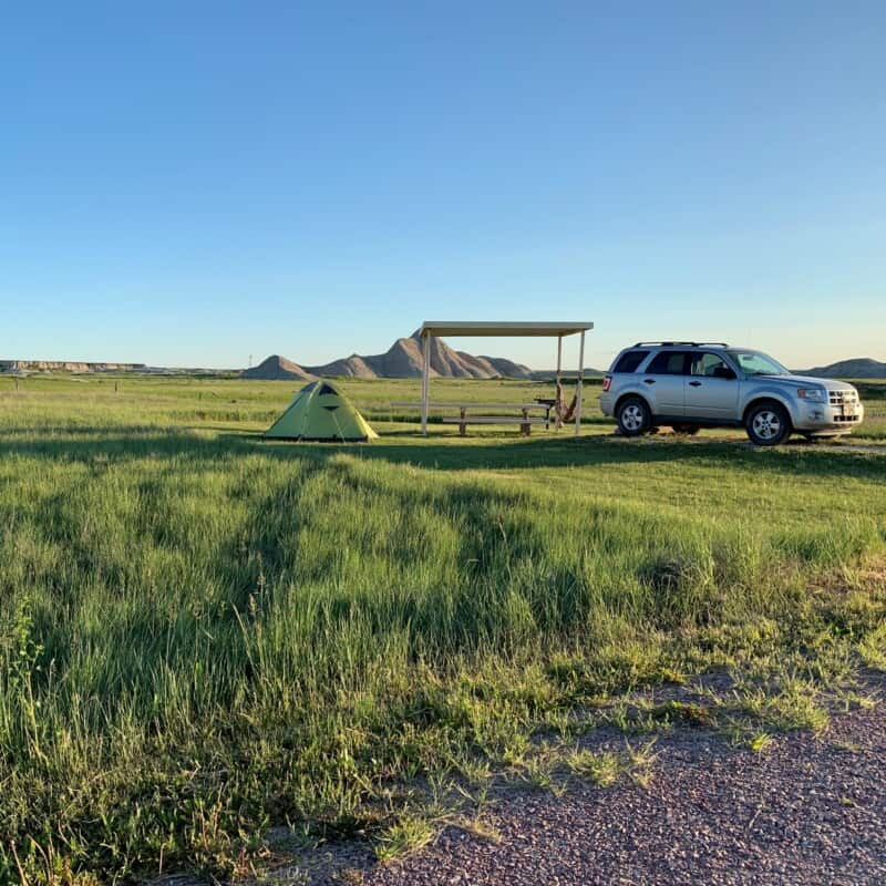 View of a campsite with a green tent, a covered picnic table, and a silver SUV at the grasslands in Nebraska