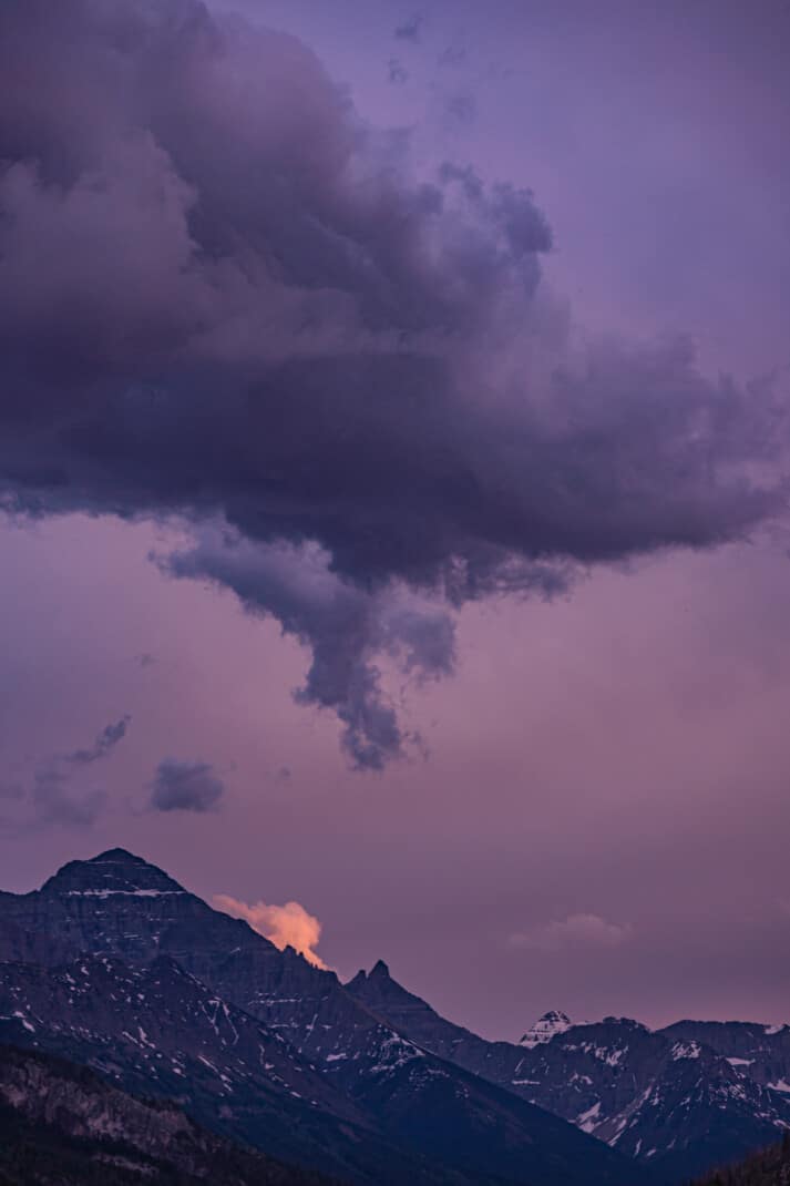Moody cloud set in a purple sky over sharp snowy mountain peaks in Waterton Lakes National Park.